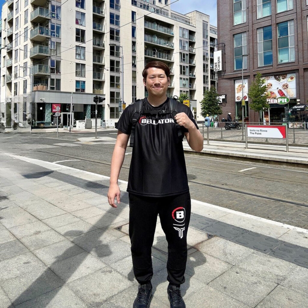 BELLATORロゴ入りウェアを着て街を歩くトレーナー加藤。計量日も現地で選手を支える