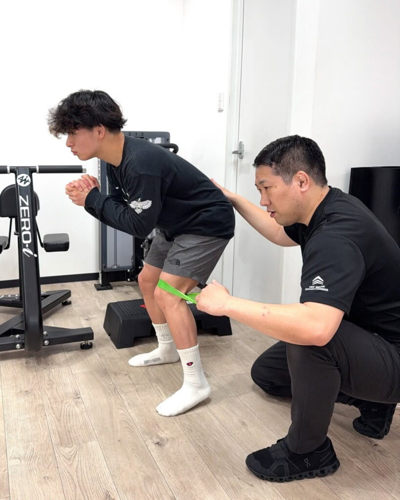 レスリング選手がコンディショニング目的で股関節の動作トレーニングを受けている様子。ZERO-i設備のある空間での指導。