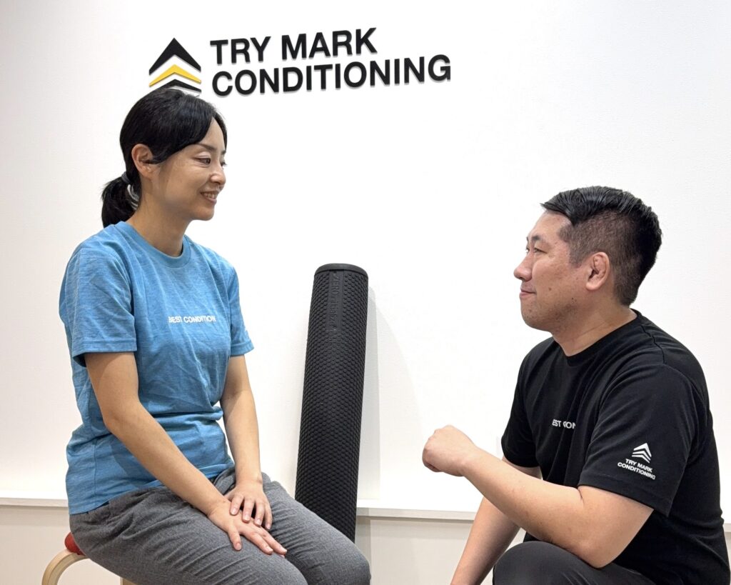 アクティブストレッチ施術後、女性が笑顔でリラックスしながらトレーナーと向き合って会話している様子。