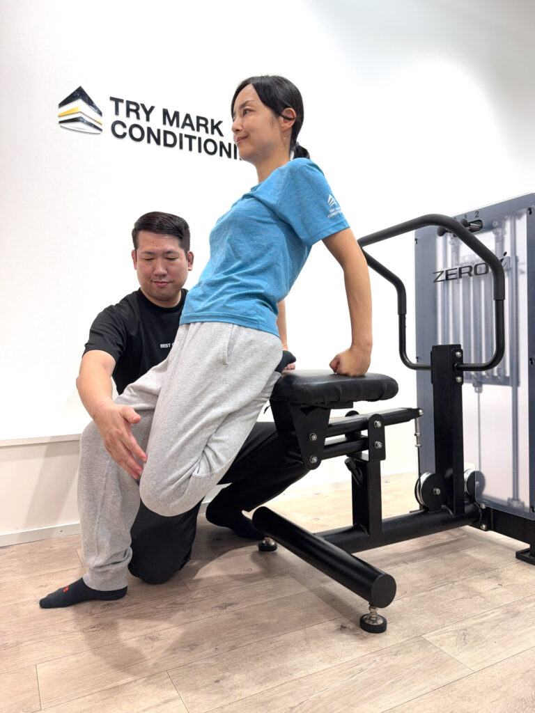 ZERO-iマシンを使い、女性が後ろに反りながら胸と腰をストレッチしている様子。トレーナーが足を支えている。