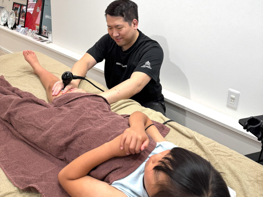 小学生の空手女子アスリートが試合前の足の疲労ケアを受けている様子。ラジオ波を使った施術中のシーン。