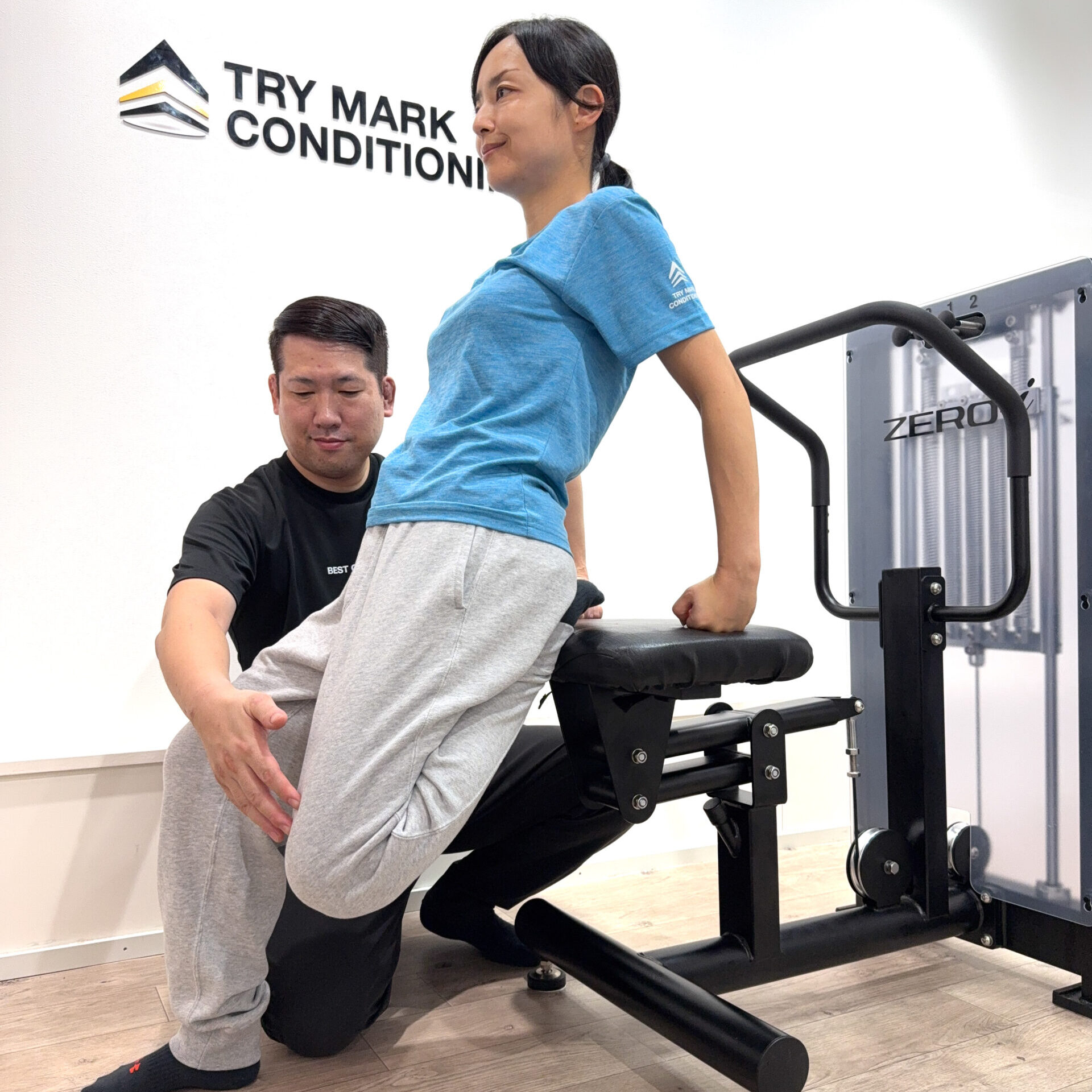 ZERO-iマシンを使い、女性が後ろに反りながら胸と腰をストレッチしている様子。トレーナーが足を支えている。