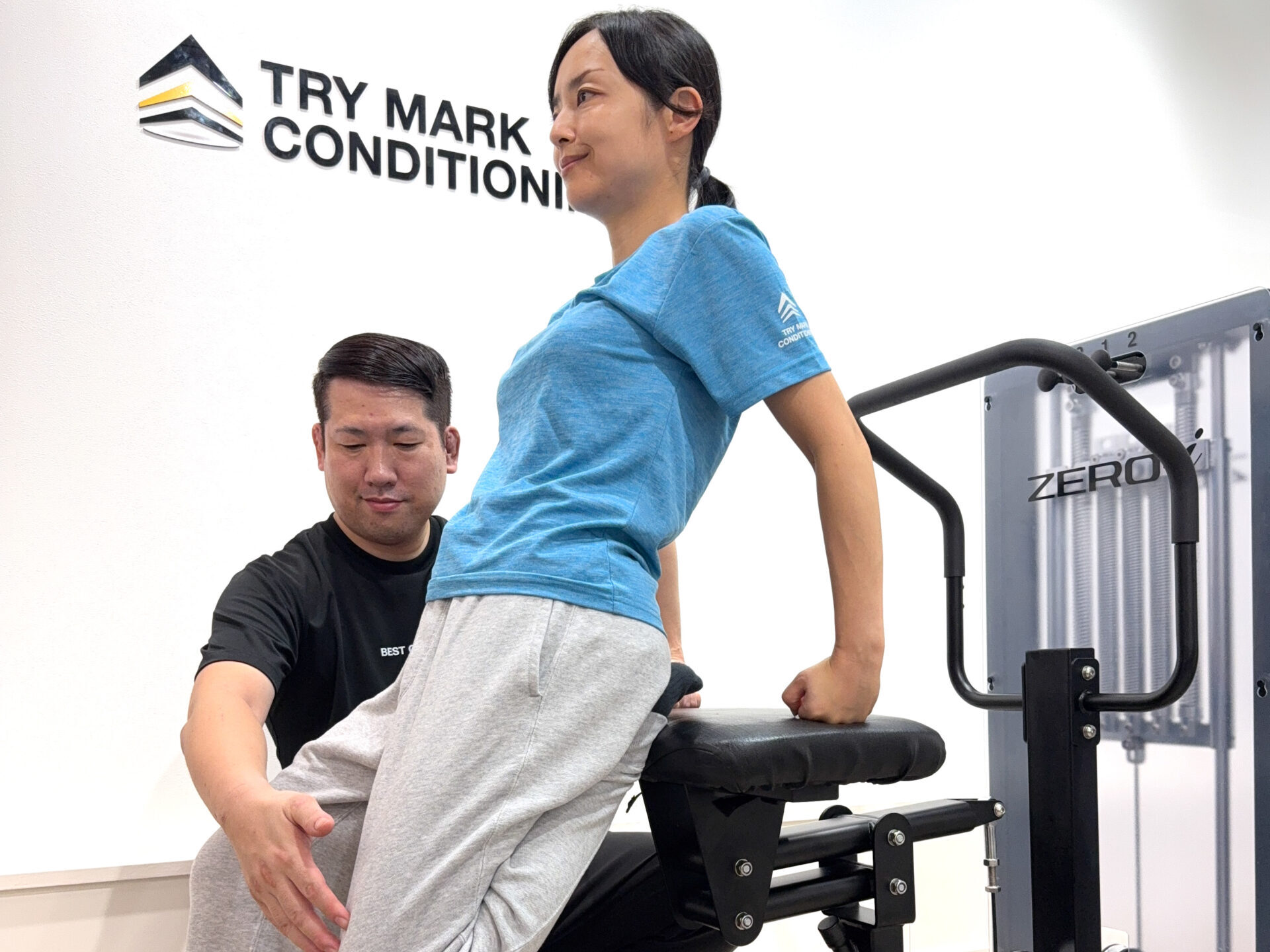 ZERO-iマシンを使い、女性が後ろに反りながら胸と腰をストレッチしている様子。トレーナーが足を支えている。